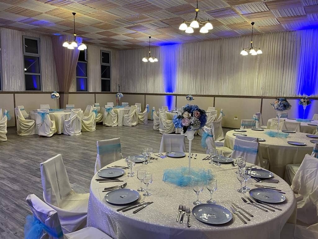 Vedere de ansamblu a salonului de evenimente aranjat, cu mese rotunde și tavan de lemn