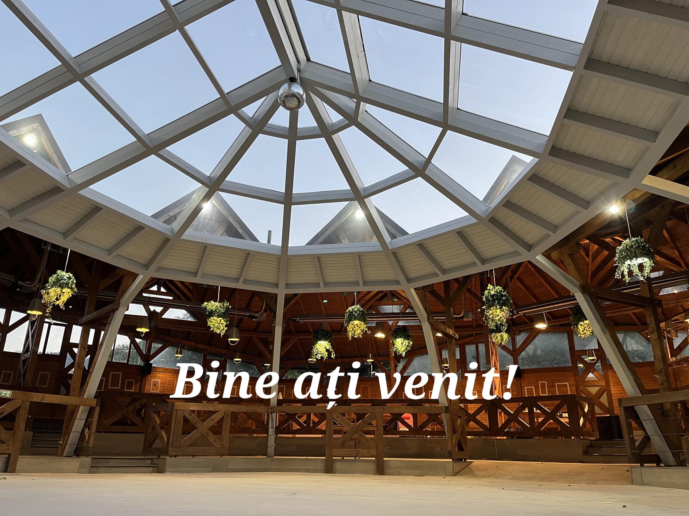 Cupola de sticlă a foișorului All Time Events din Brașov, văzută de jos, cu grinzi de lemn și ghivece suspendate