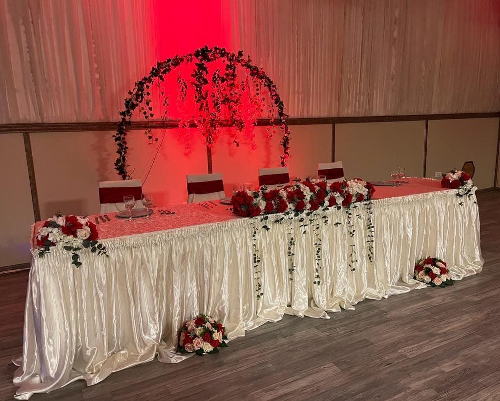 Prezidiu de nuntă cu arcadă florală și aranjamente de trandafiri roșii, pe fundal de draperii iluminate în roșu